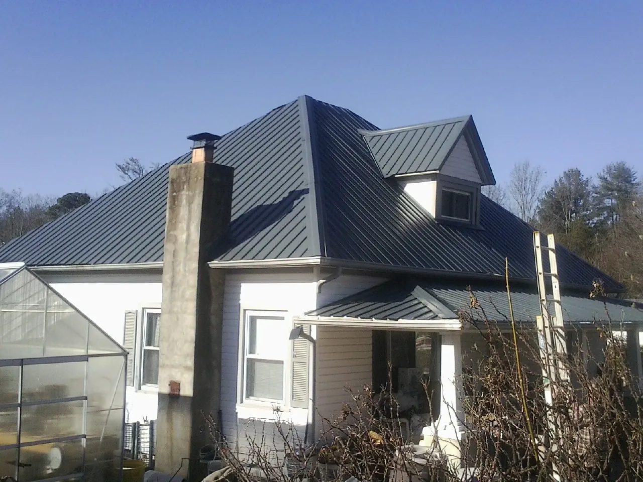 Dark blue standing seam metal roof on a white farmhouse with dormer — Slate & Tile Roof Repair by Roofing Brothers in Nevada