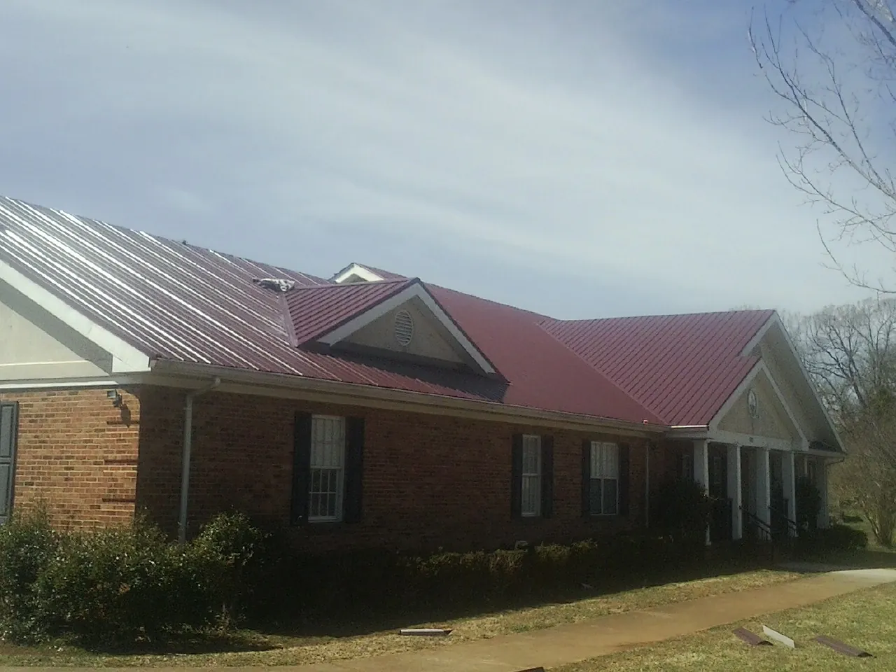 Red metal roof with gabled entries on a long brick building, from a Hail Damage Roof Repair job in Nevada