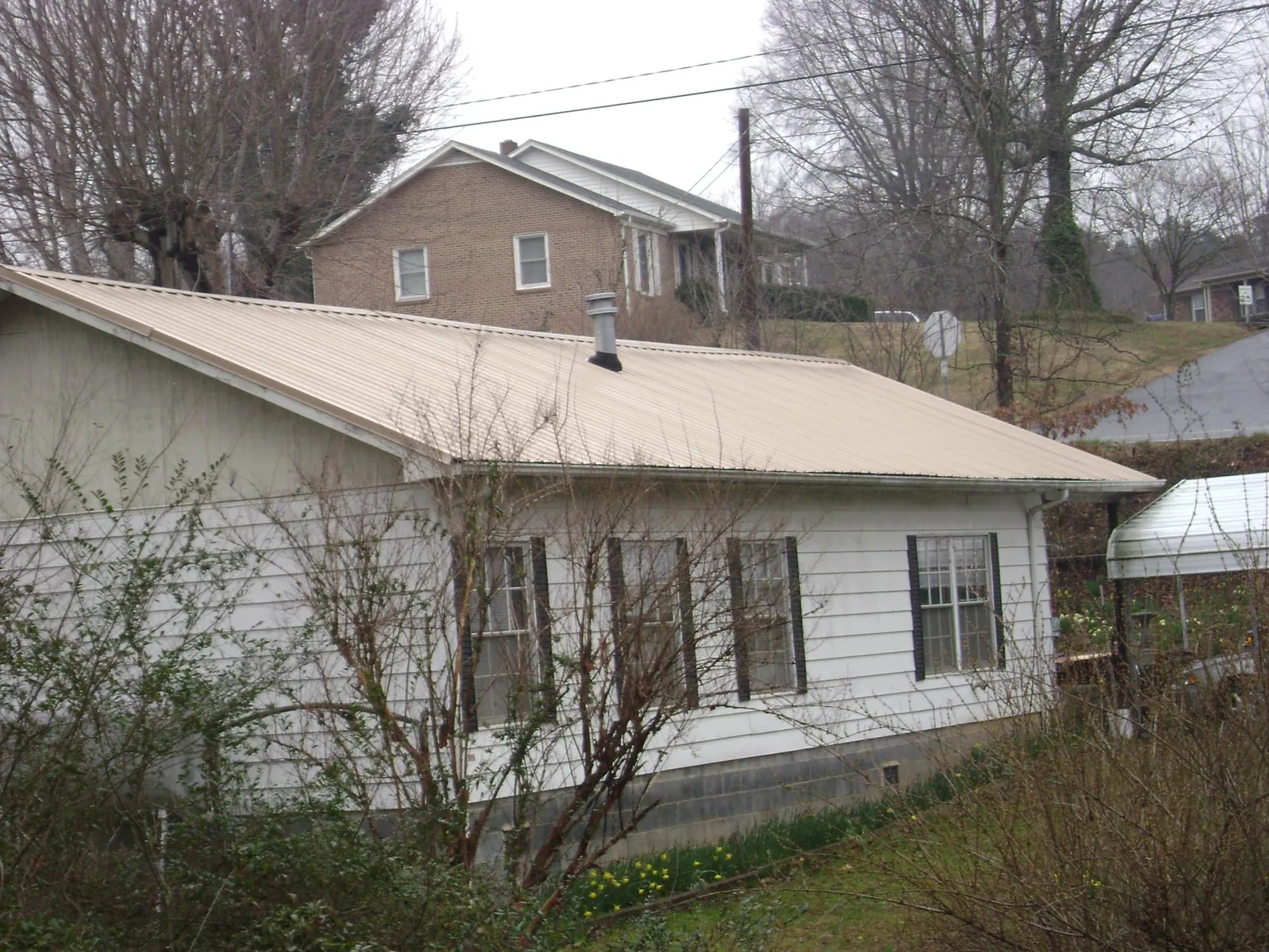 Tan metal roof on a white sided house set into a hillside — Commercial Roofing by Roofing Brothers in Nevada
